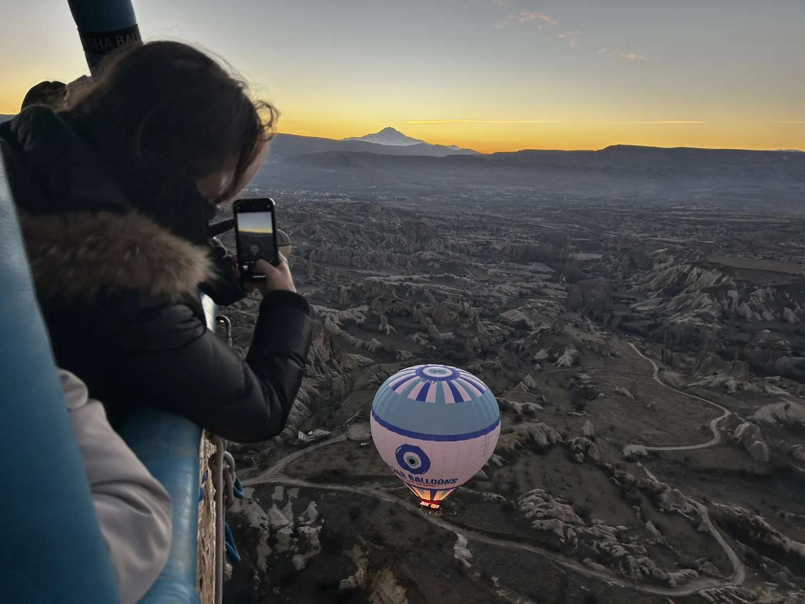 Tourist looking out over Cappadocia and Nazar balloon from the basket on a hot air balloon